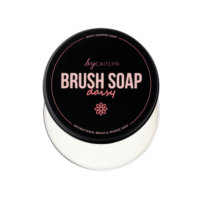 Container of brush soap with a black lid featuring pink text on a white background
